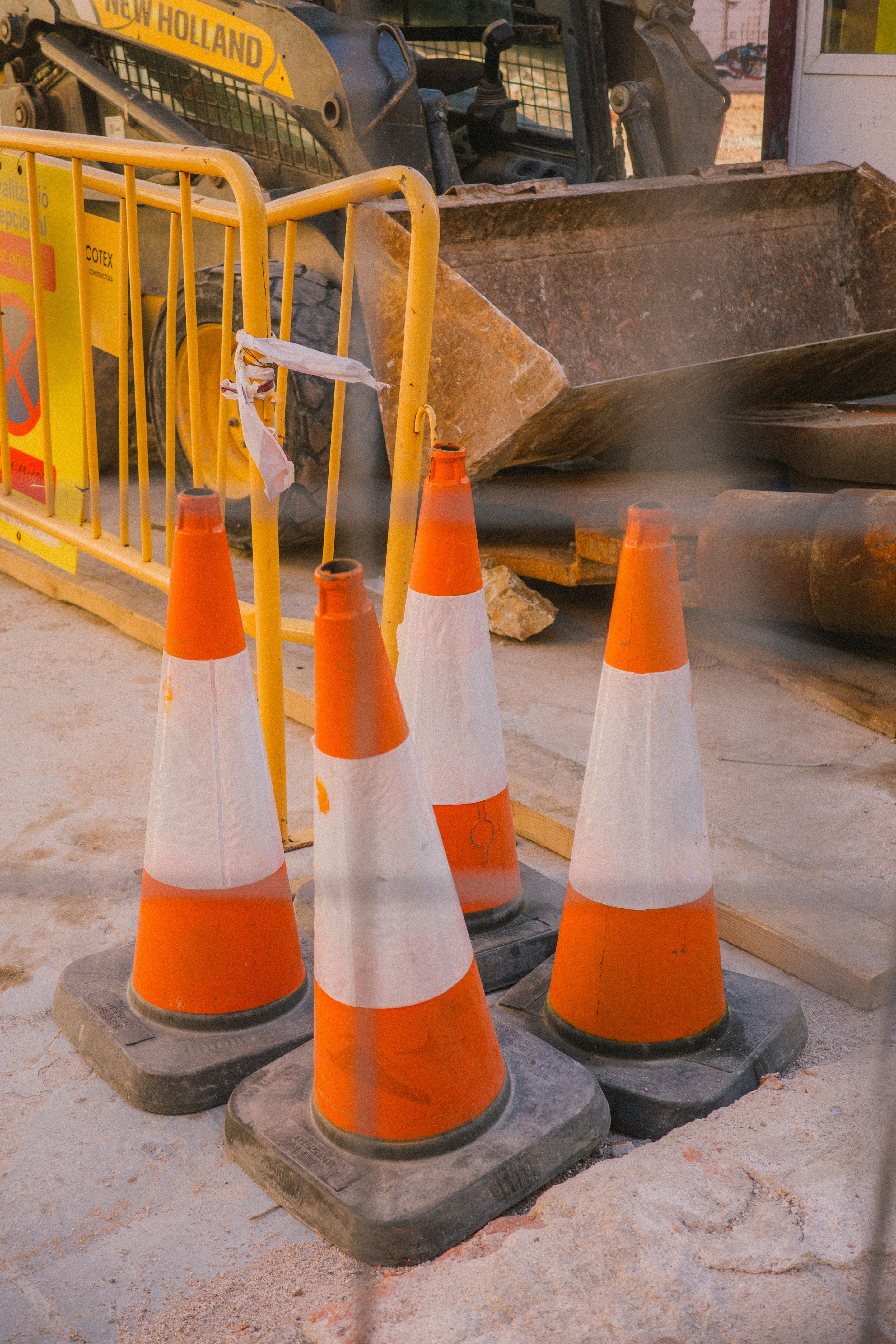 Foto de cuatro conos en el interior de una obra. Detrás de los conos hay una excavadora.