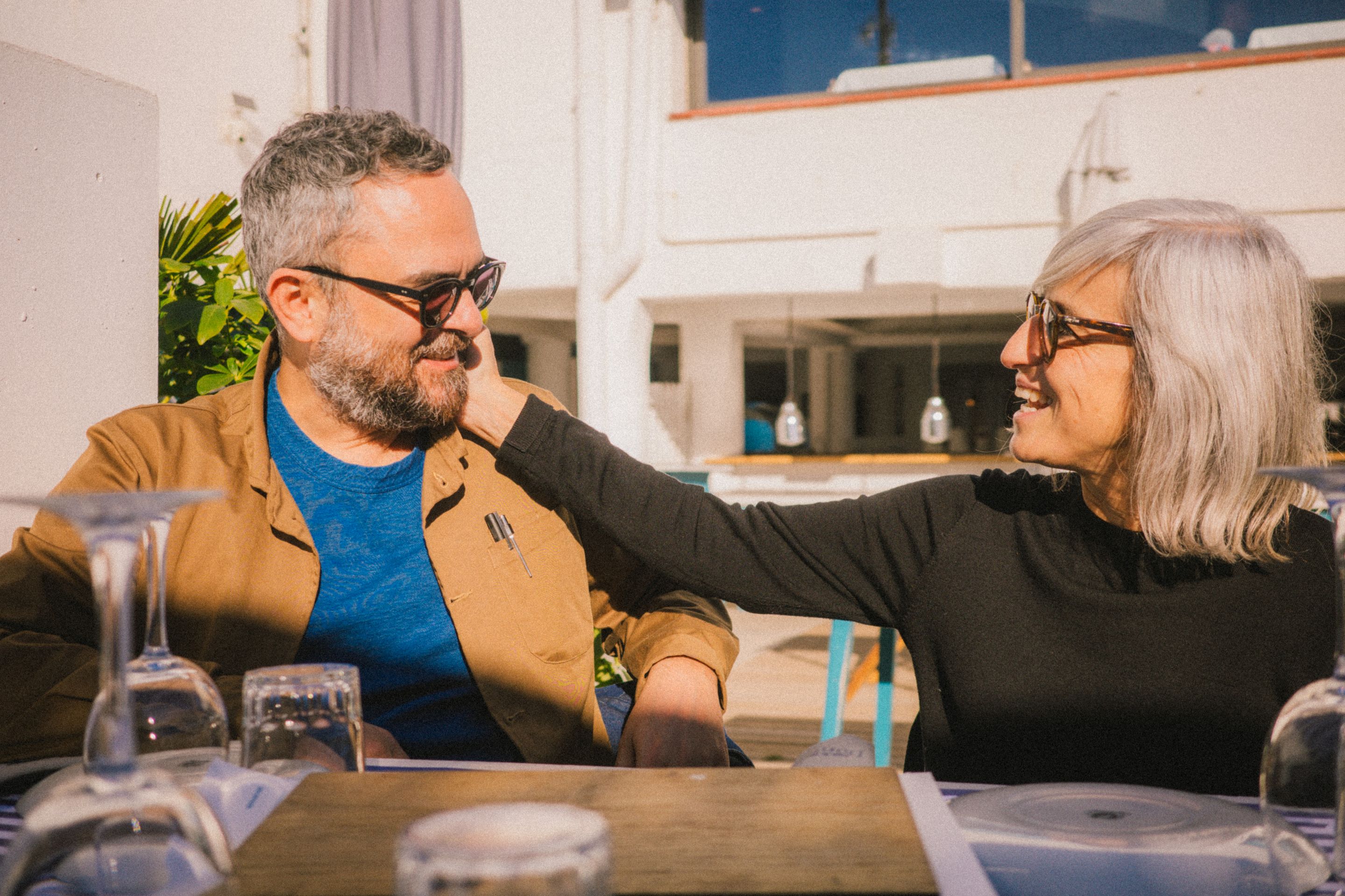 Retrato de Orlando y Laura sentados a la mesa del restaurante mirándose el uno al otro. Laura le está tocando la mejilla a Orlando.